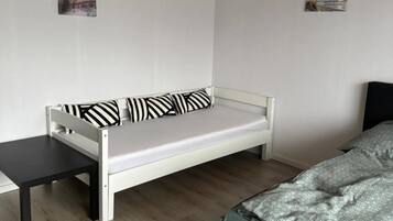 Una habitación con un sofá blanco, una mesita, una cama con colcha estampada y dos cuadros colgados en la pared.
