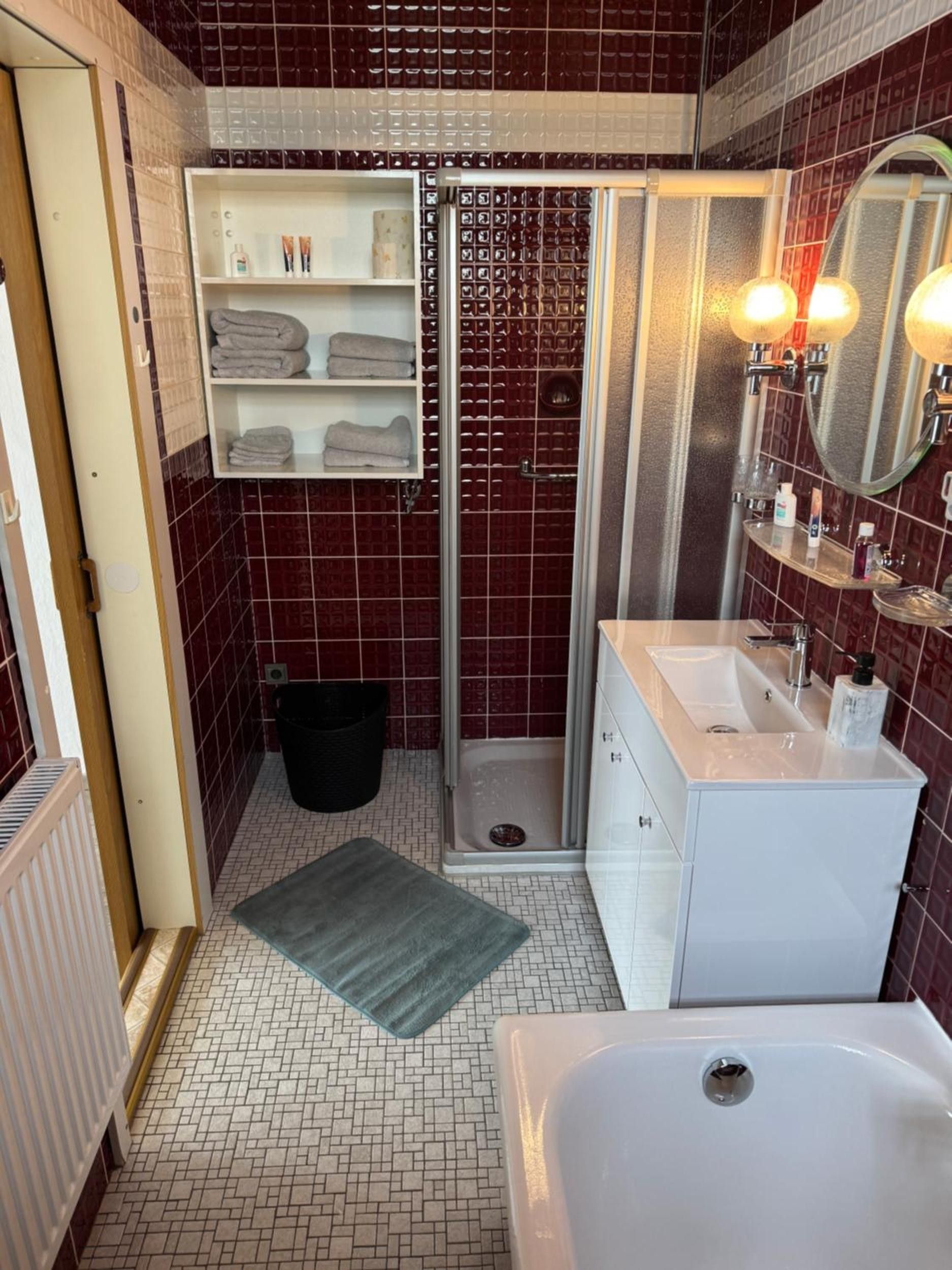 Un baño con ducha, lavamanos, espejo y perchero para toallas.