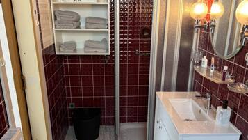 Un baño con ducha, lavamanos, espejo y perchero para toallas.