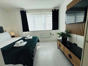 A hotel room with a bed, bedside table, lamp, potted plant, and a large mirror. - 
Modern Executive Studio 11 | Central Swindon (Swindon)