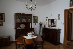 Uma sala de jantar com mesa de madeira, cadeiras, um lustre e um armário com objetos decorativos.