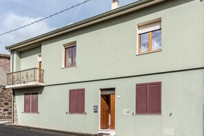 Um edifício de dois andares com varanda, persianas e porta.