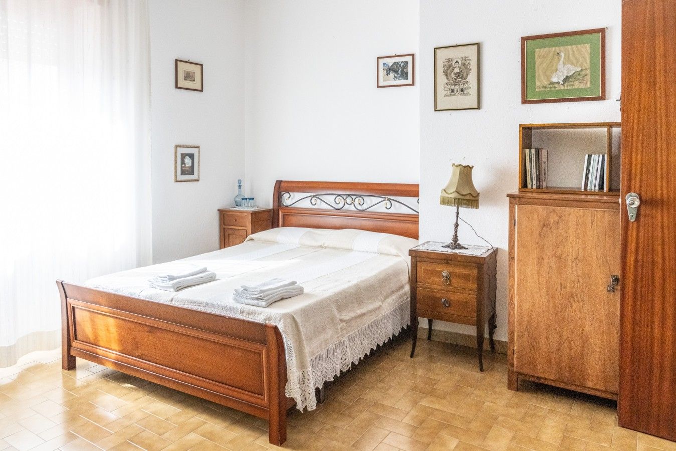 Quarto com cama de madeira, mesas de cabeceira, abajur, guarda-roupa e quadros na parede.