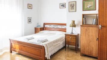 Quarto com cama de madeira, mesas de cabeceira, abajur, guarda-roupa e quadros na parede.