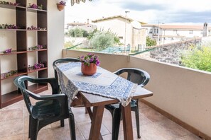 Varanda com mesa e cadeiras, um vaso de planta e vista para edifícios e vegetação.