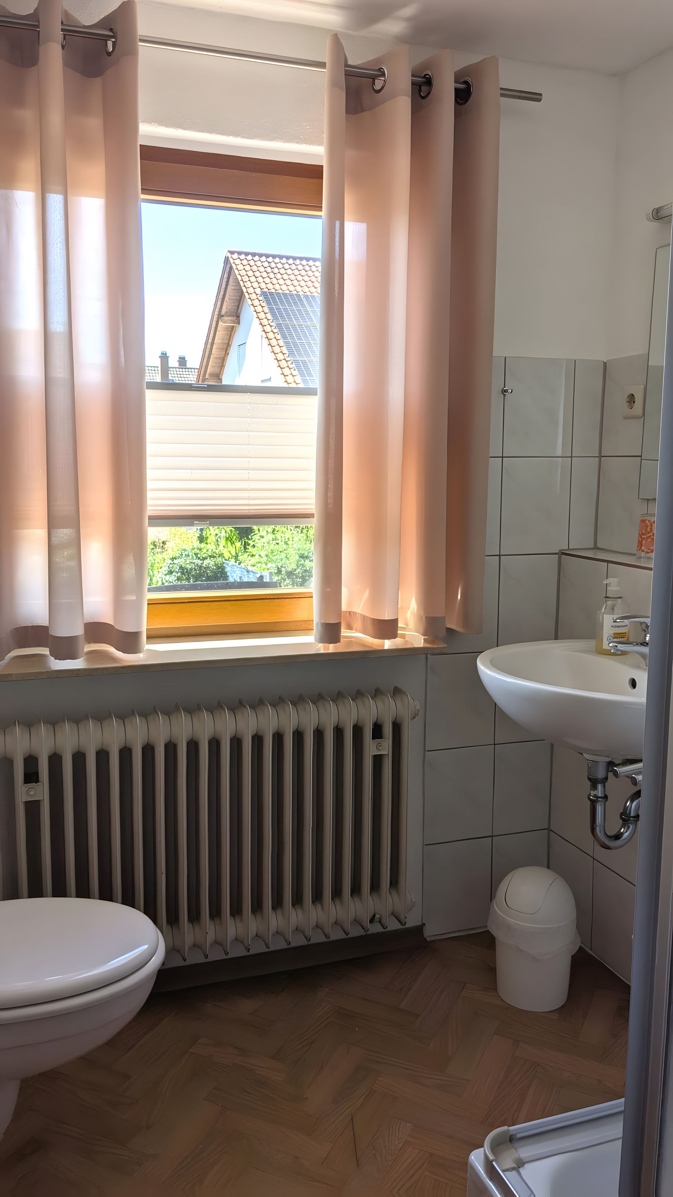 Ein Badezimmer mit Toilette, Waschbecken, Heizkörper und einem Fenster mit Vorhängen.