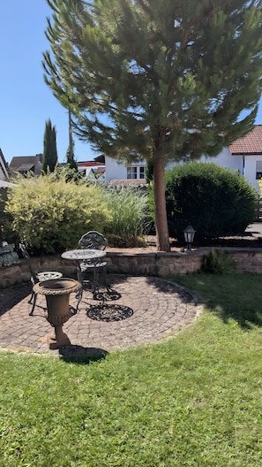 Ein Garten mit einer Terrasse, einem Tisch und Stühlen, umgeben von einer Steinmauer und verschiedenen Pflanzen.