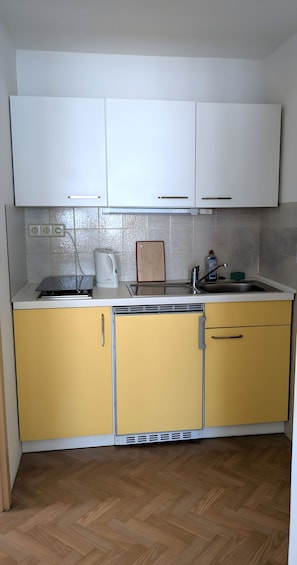 Eine kleine Küche mit weißen Oberschränken, gelben Unterschränken, einem eingebauten Backofen und einer Edelstahl-Spüle.