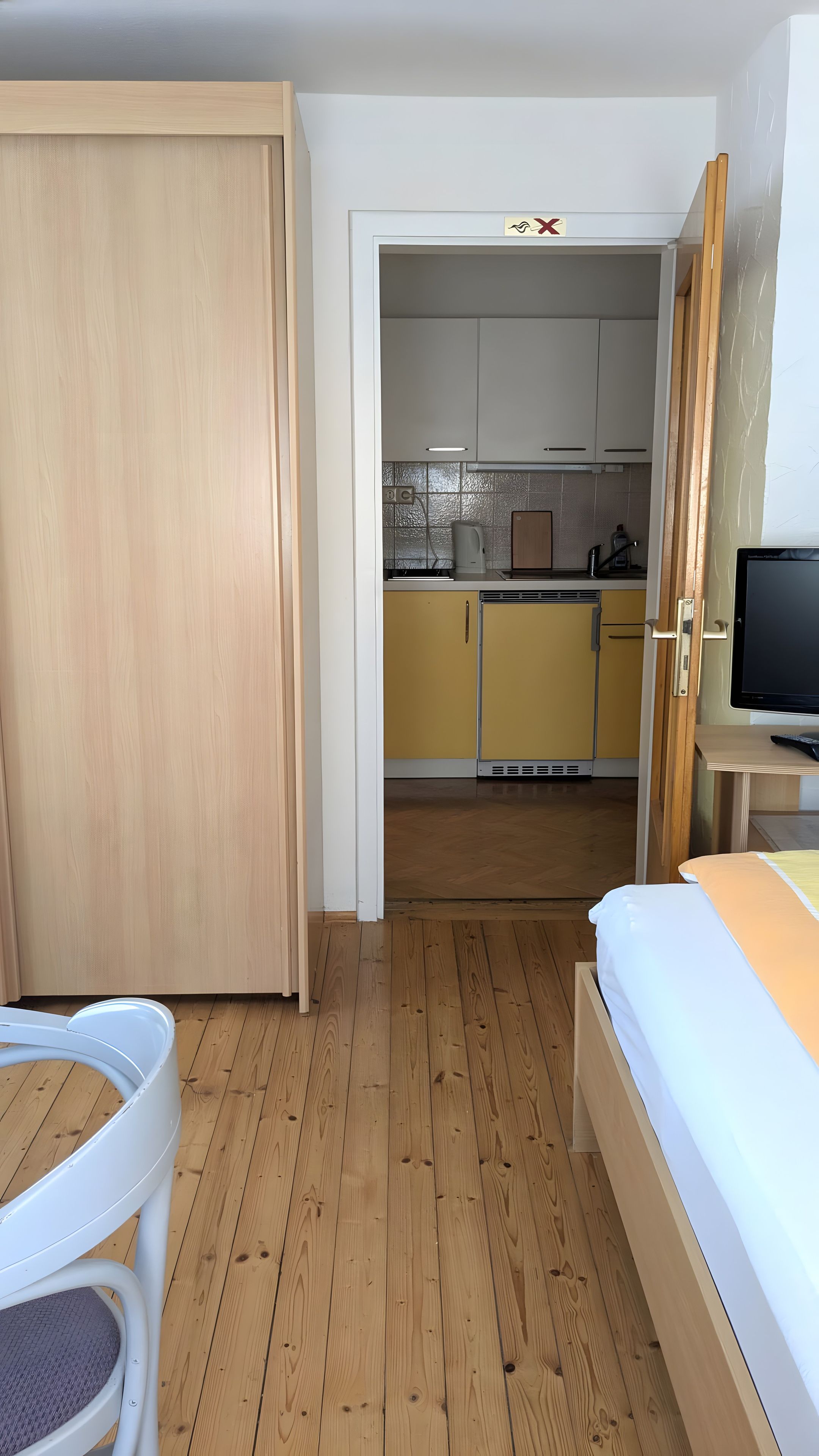 Ein Zimmer mit einem Bett, einem Sessel, einem Fernseher und Blick in einen Küchenbereich.