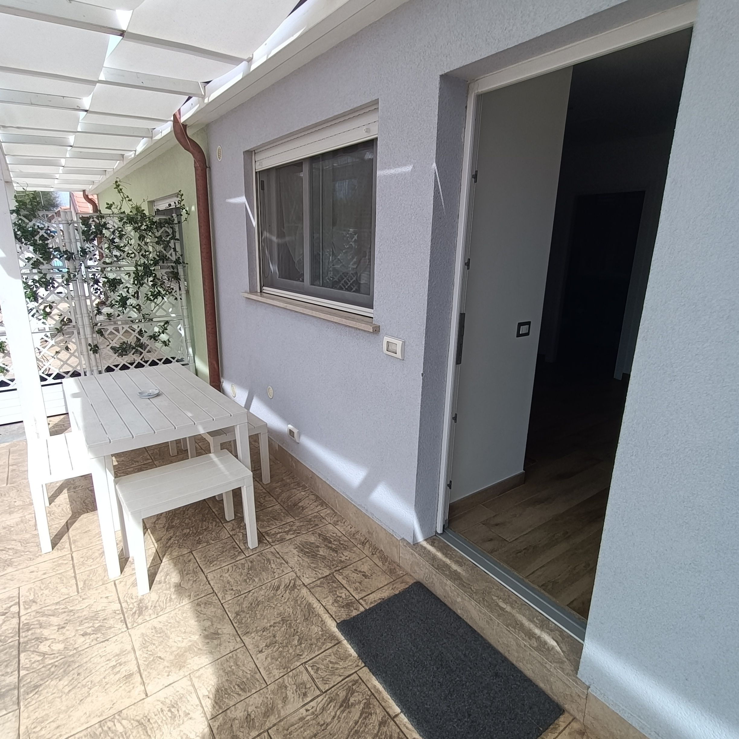 A patio area with a white table and bench, a window, and a door leading to an interior space.