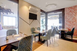 Un espace de salle à manger moderne, avec une longue table, de nombreuses chaises et un téléviseur à écran plat fixé au mur.