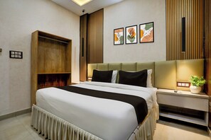 A modern hotel room with a large bed, a bedside table with a lamp, a small plant, and a wall-mounted shelf. - OYO Collection O George Town (Prayagraj)