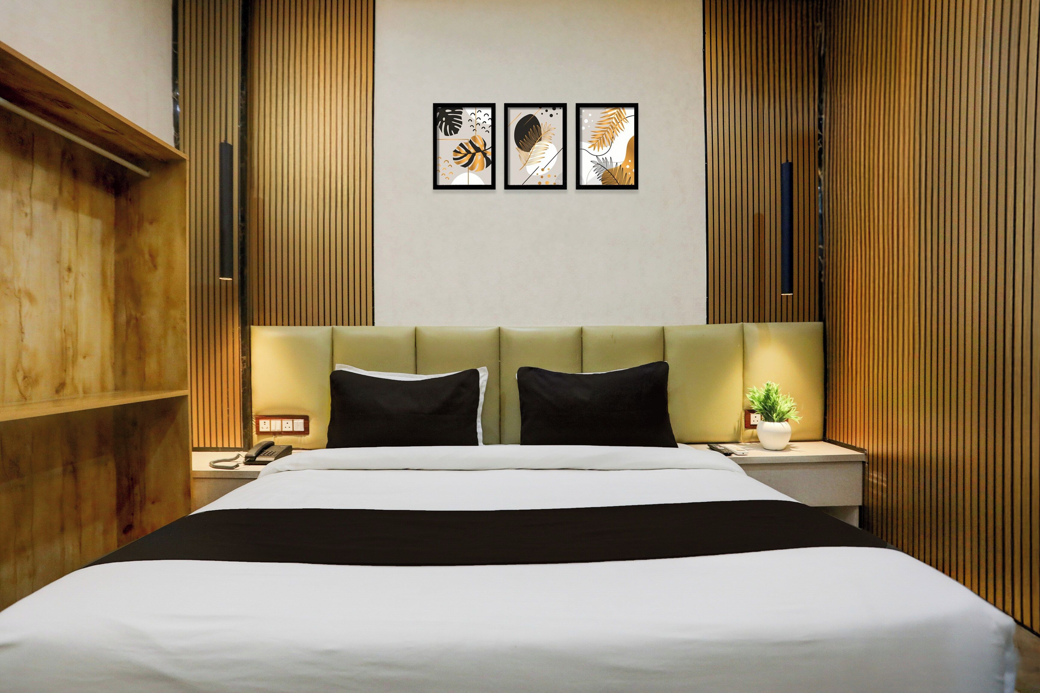 A hotel room with a large bed, two bedside tables, a nightstand, a wall-mounted telephone, and three framed artworks above the bed.