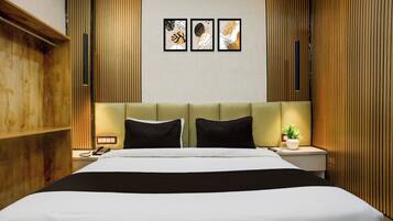 A hotel room with a large bed, two bedside tables, a nightstand, a wall-mounted telephone, and three framed artworks above the bed.
