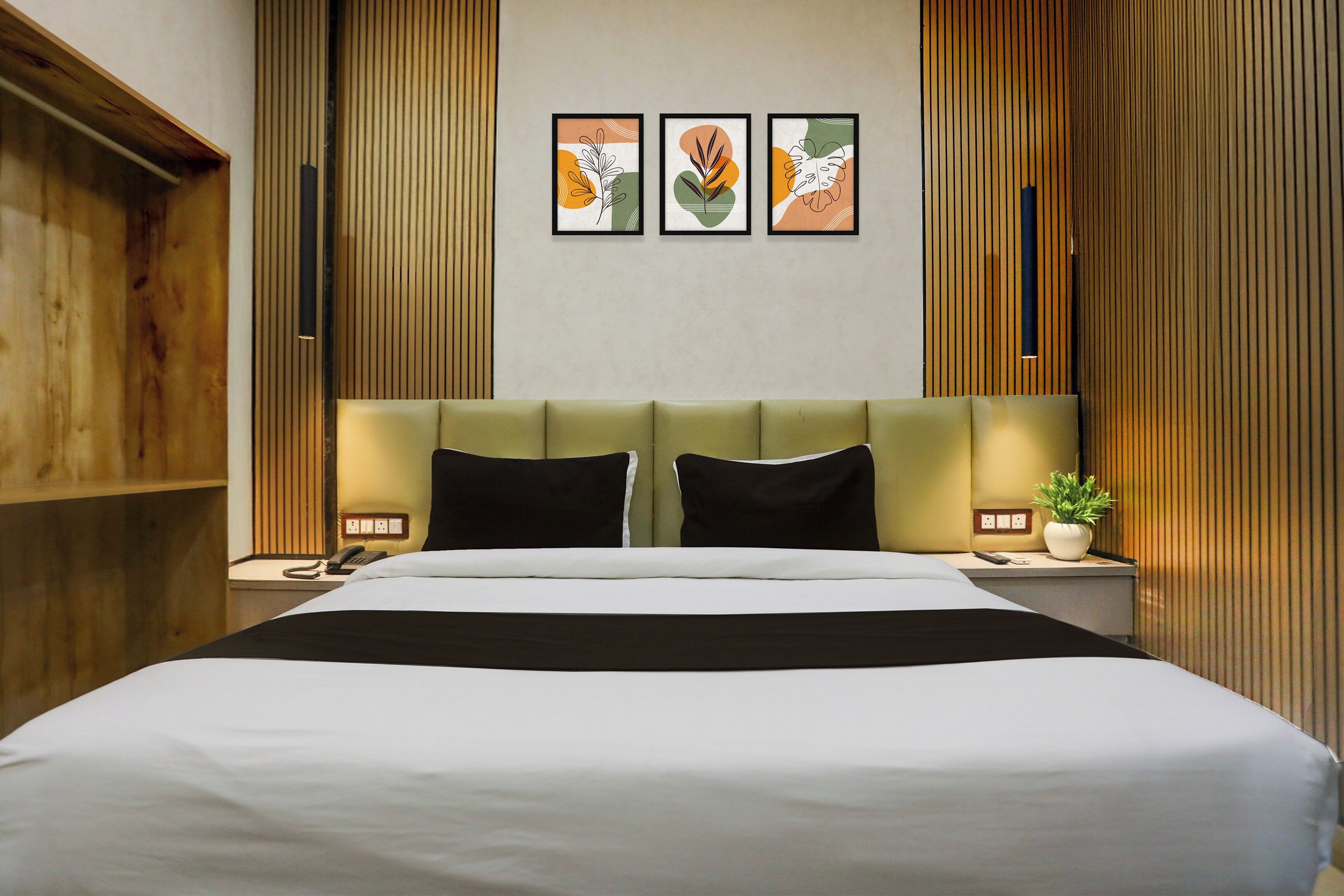 A hotel room with a large bed, a headboard, two bedside tables, a telephone, a remote control, and a potted plant.