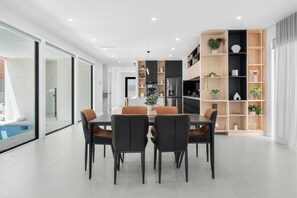 Een moderne eetruimte met glazen wand, uitzicht op een zwembad en een keuken met inbouwapparatuur.