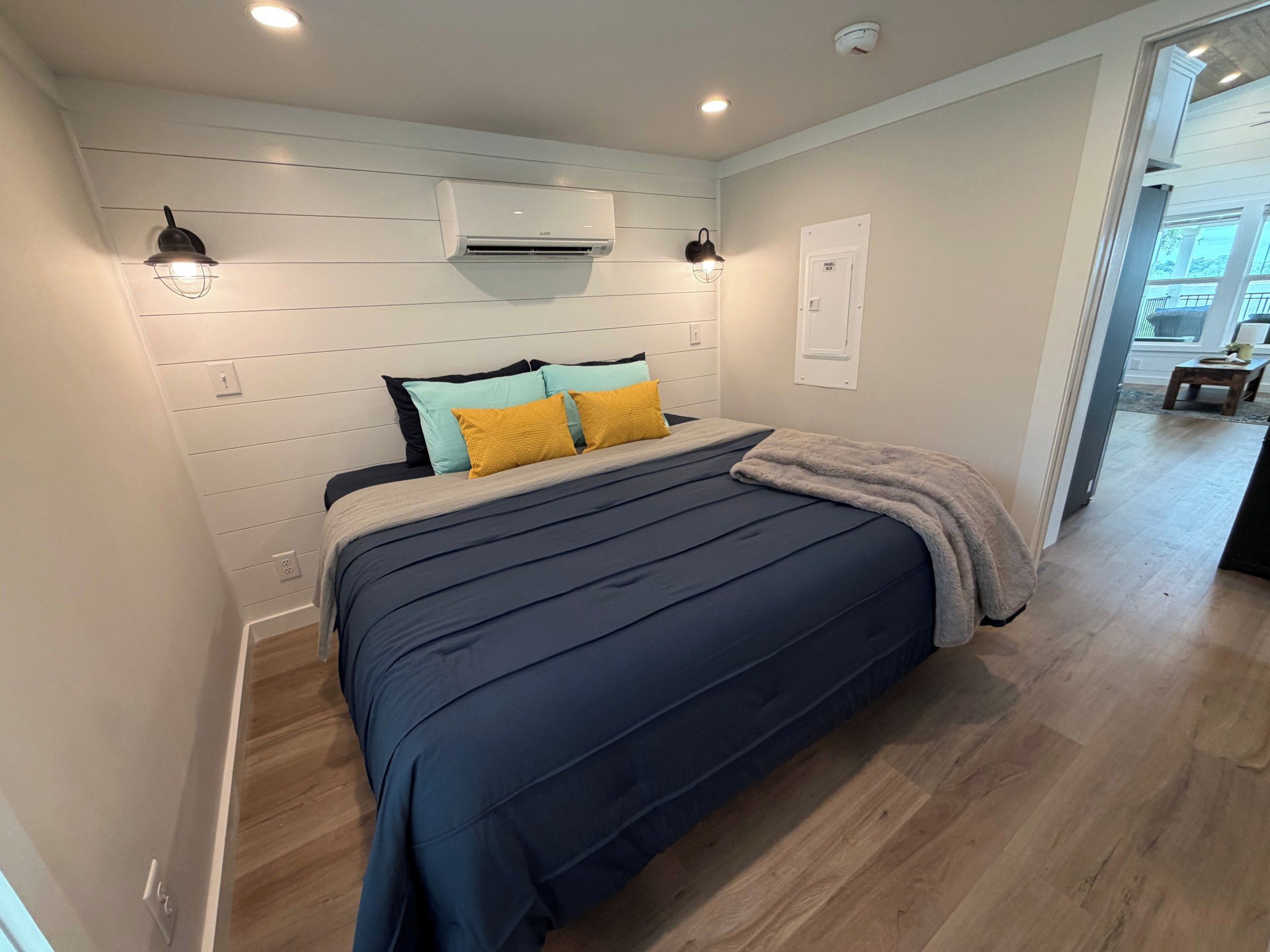 Un dormitorio con una cama, aire acondicionado de pared y una puerta a otra habitación.
