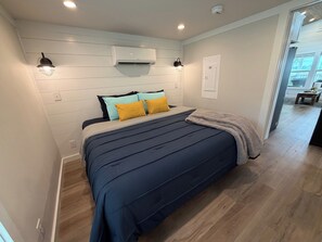 Un dormitorio con una cama, aire acondicionado de pared y una puerta a otra habitación.