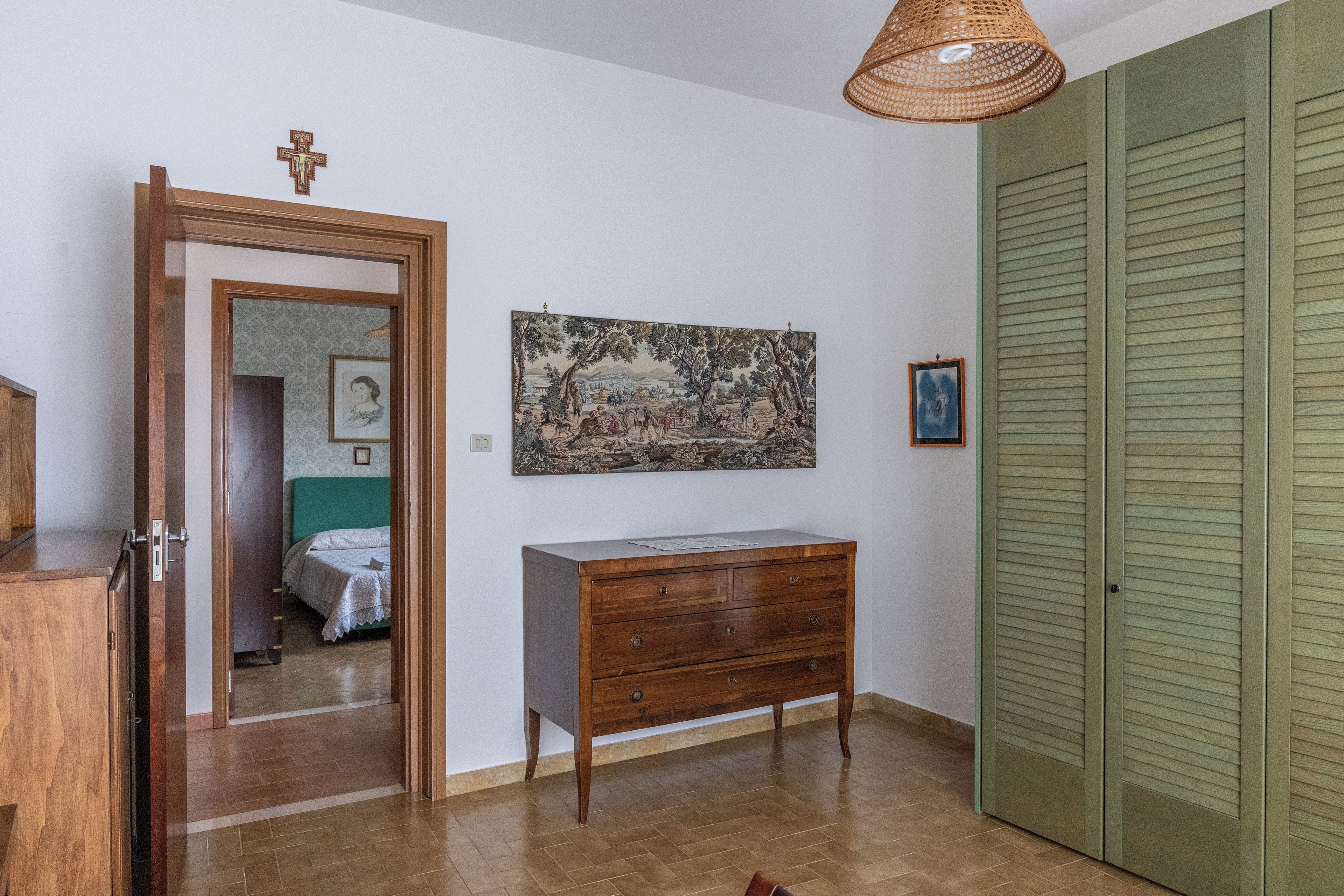 A room with a wooden dresser, a painting on the wall, a door, and a green closet.