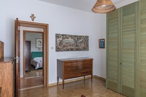 Una stanza con una cassettiera in legno, un quadro appeso al muro, una porta e un armadio verde.