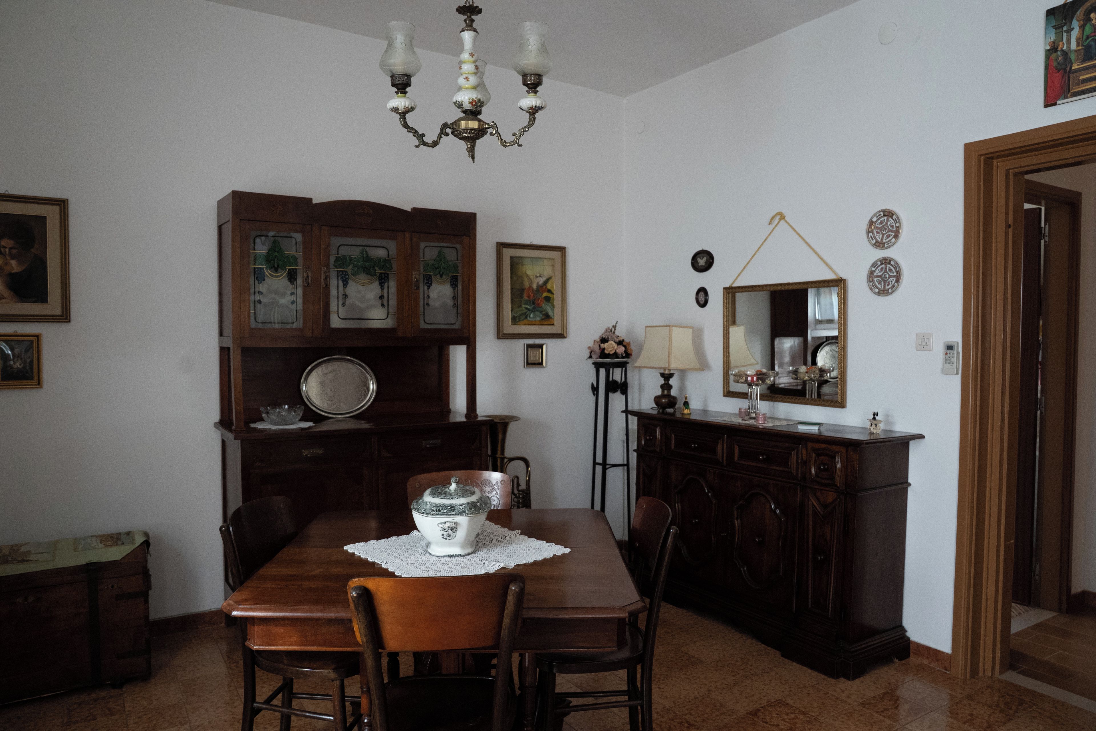 A dining area with a wooden table, chairs, a chandelier, and a cabinet with decorative items.