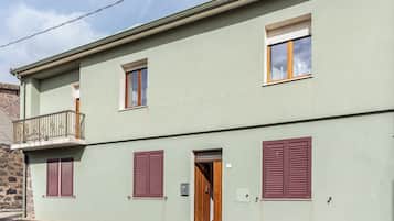 A two-story building with a balcony, shutters, and a door.