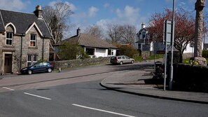 Une route sinueuse, une maison en pierre et une voiture garée.