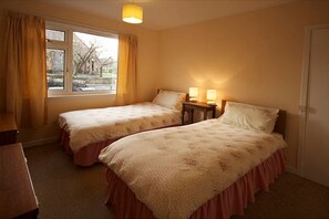 Une chambre avec deux lits, une fenêtre avec des rideaux et une table de chevet avec des lampes.