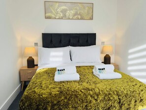 Ein Hotelzimmer mit einem Bett, zwei Nachttischlampen, einem Wandbild und einem ordentlich bezogenen Bett mit Handtüchern und Pflegeartikeln.