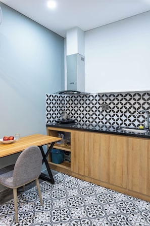 A compact kitchen with a wooden table, a chair, a kettle, and a sink. - LEE NÔM VILLA DANANG (Ngũ Hành Sơn)