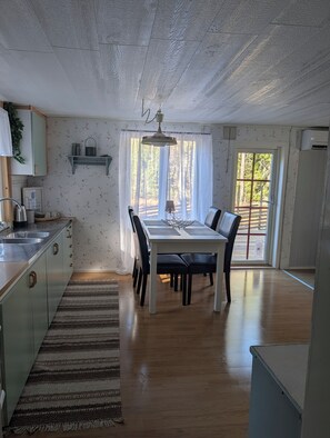 A dining area with a table and chairs, a kitchen with a sink, and a window with curtains. - Lillhamra Cottage, in the heart of swedish nature (Lillhamra)