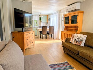 A living room with a sofa, a television, a wooden cabinet, and a dining area with chairs and a table. - Lillhamra Cottage, in the heart of swedish nature (Lillhamra)