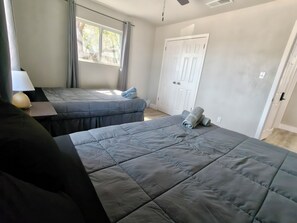 Quarto com duas camas, uma escrivaninha, abajur e janela com cortinas.