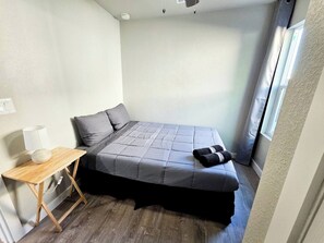 Un dormitorio pequeño y ordenado con cama, mesita de noche y ventana.