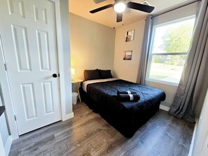 Un dormitorio con una cama, un ventilador de techo, una ventana con cortinas y una puerta.