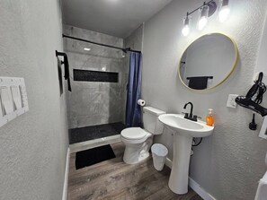 Un baño con ducha, inodoro, lavamanos y espejo.
