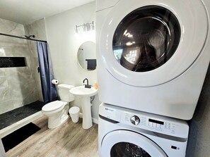 Un baño moderno con lavadora y secadora integradas, inodoro, lavamanos y zona de ducha.
