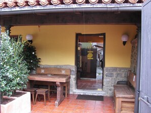Um pátio externo com mesa e bancos de madeira, um vaso de plantas e uma parede de pedra.