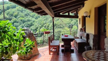 A covered patio with a table and chairs, a stone planter, and a view of a forested hillside.
