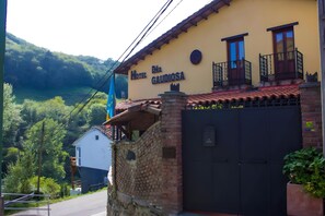 Um hotel chamado 'Hotel Digna Galidosa' com entrada por uma parede de tijolos, uma varanda com guarda-corrimão preto e vista para um vale verdejante.
