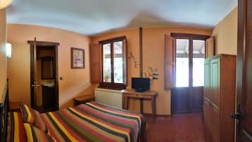 A bedroom with a bed, a television on a desk, and a window with blinds.