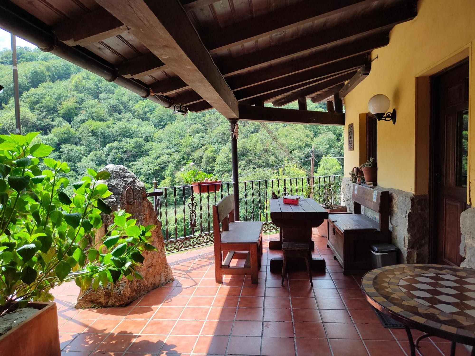 A covered patio with a table and chairs, a stone planter, and a view of a forested hillside.