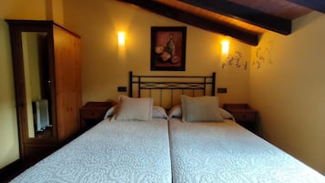 A double bed with a patterned bedspread, a wooden headboard, two bedside tables, a wall-mounted painting, and a wooden ceiling beam.