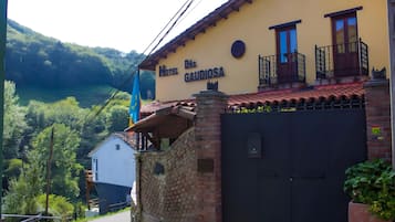 A hotel named 'Hotel Digna Galidosa' with a brick wall entrance, a balcony with a black railing, and a view of a lush green valley.