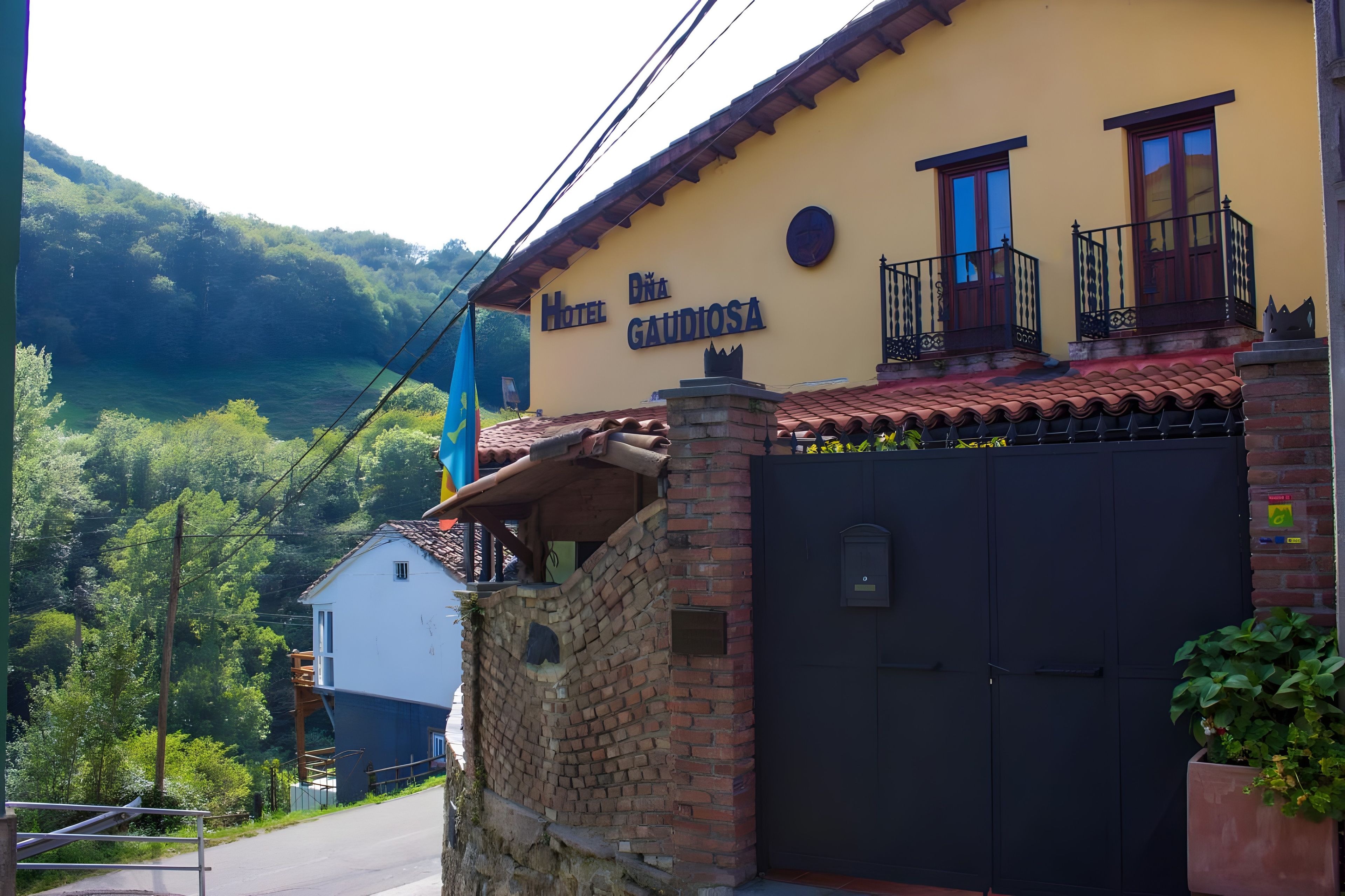 A hotel named 'Hotel Digna Galidosa' with a brick wall entrance, a balcony with a black railing, and a view of a lush green valley.