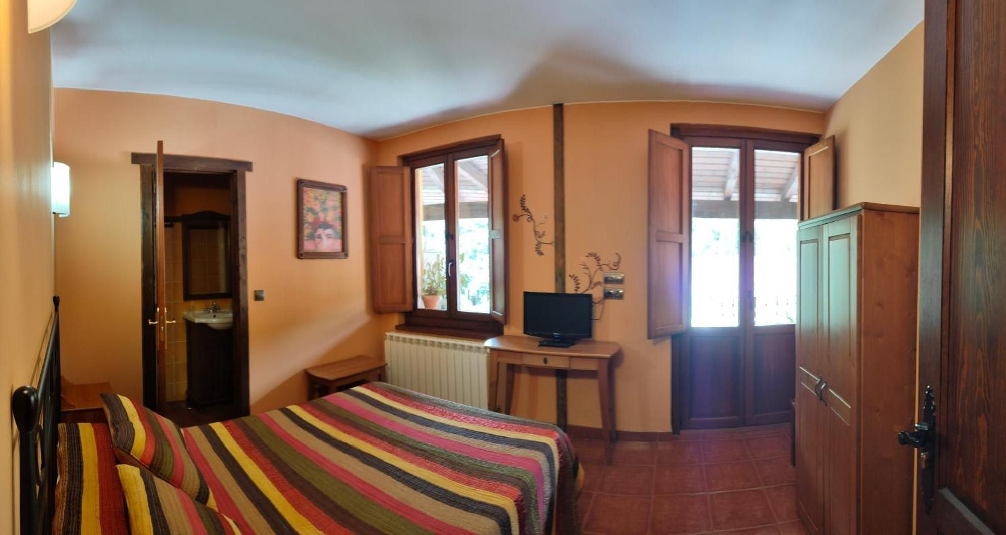 A bedroom with a bed, a television on a desk, and a window with blinds.