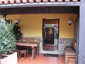 Um pátio externo com mesa e bancos de madeira, um vaso de plantas e uma parede de pedra.