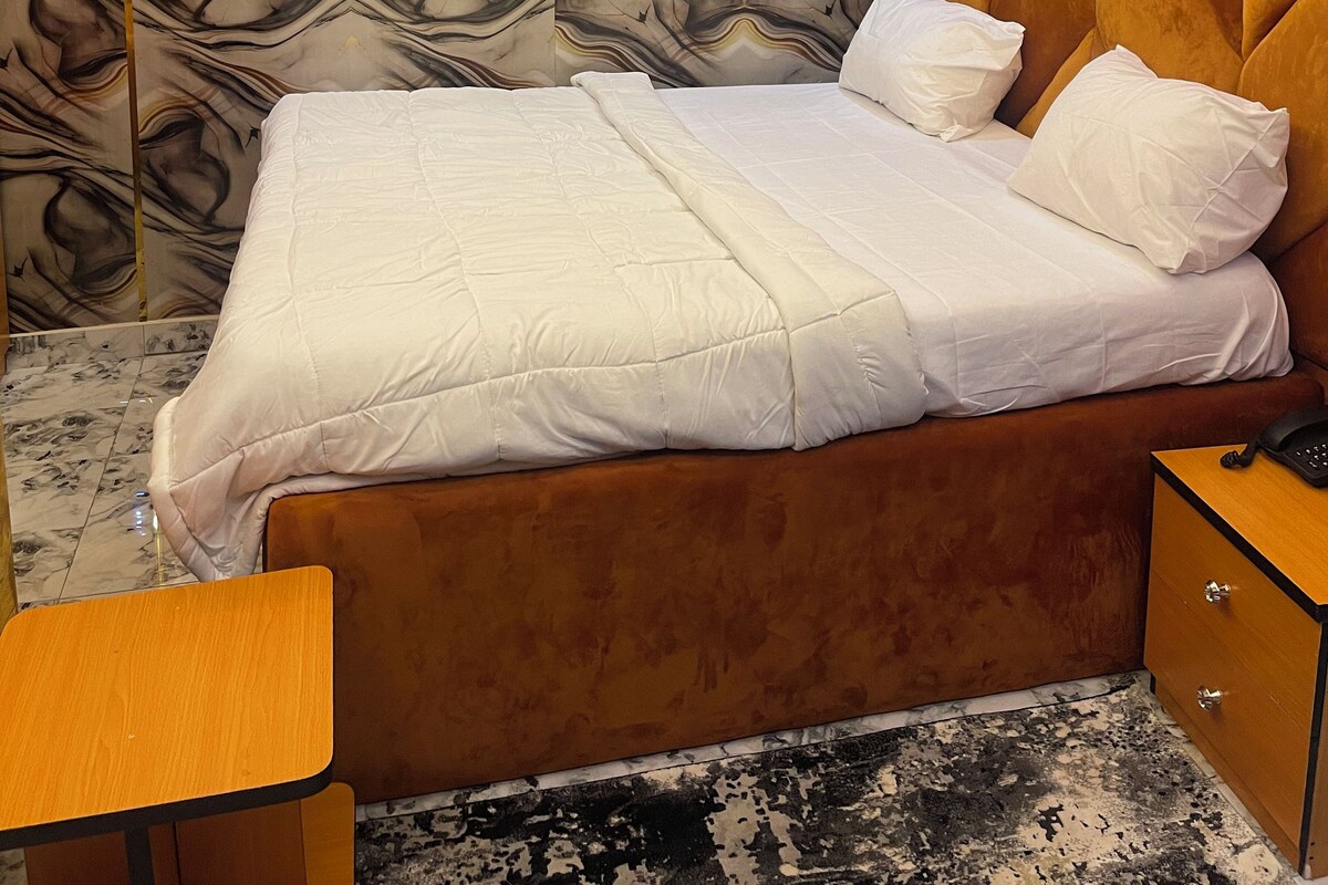 Un dormitorio con una cama, una mesita de noche de madera, un escritorio y una pared con diseño decorativo.