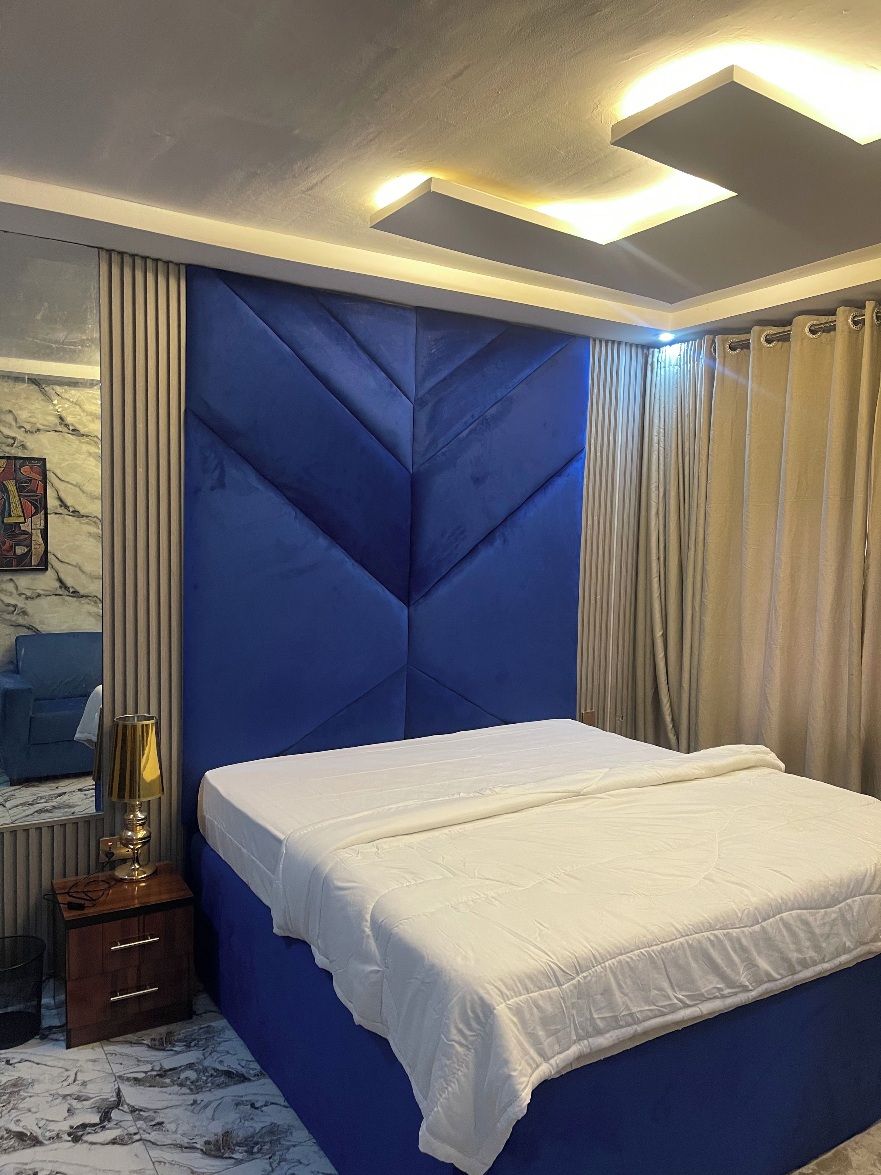 A bedroom with a bed, a nightstand, a lamp, a mirror, and curtains.