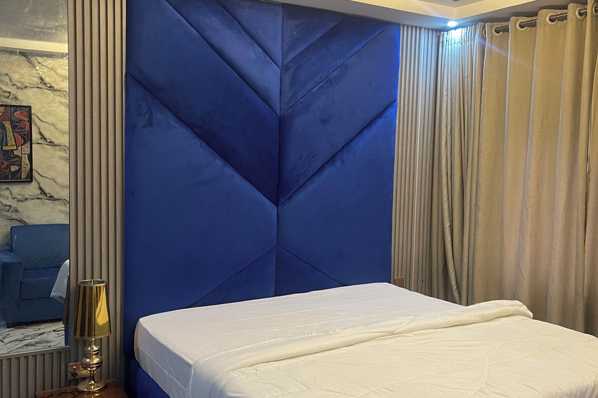 Un dormitorio con cama, mesita de noche, lámpara, espejo y cortinas.